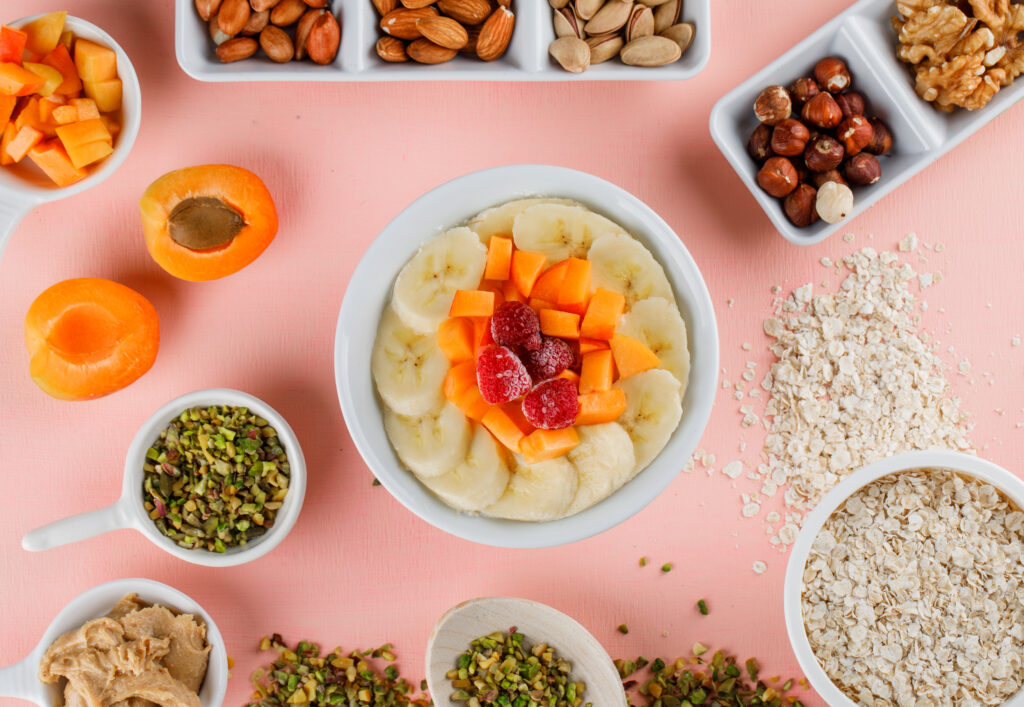 oatmeal with fruits, nuts, peanut butter, oat flakes in a bowl on pink background, flat lay.
